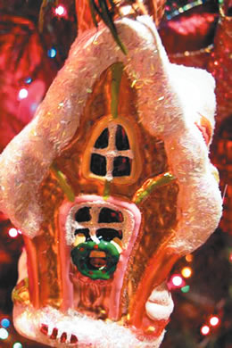 A traditional gingerbread house ornament hangs on the main tree