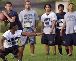 Waipahu quarterbacks Jace Kaopua (with ball) and Troy Matautia (squatting) play in a summer league scrimmage against Moanalua, while players and coaches watch. Photo by Byron Lee