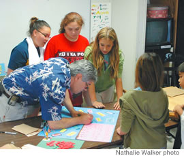 Salza signs a birthday card for a teacher as students (from left) Melissa Phillips, Stephanie Dobbs and Kylie Watanabe look on